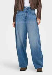 Blugi din denim ușor albastri, cu croi larg și talie înaltă, având un aspect decolorat și un stil cu cinci buzunare, completat de bocanci maro până la gleznă.