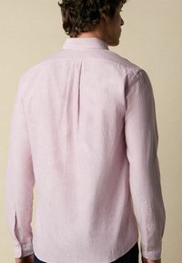 Lange mouw shirt in lichtroze met witte strepen. Beschikt over een button-down kraag, knoopmanchetten en een verticale plooi aan de achterkant. Gemaakt van katoen.