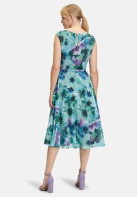 Floral A-Linie Kleid in Aquamarin mit lila und grünen Mustern, Kappärmel, Taillengürtel und Knopfdetail im Rücken. Tragen mit lila Blockabsätzen.