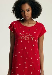 Czerwona sukienka krótki rękaw z złotym napisem "JOLLY" i rozsianymi wzorami białych i złotych płatków śniegu. Miękka tkanina o luźnym kroju.