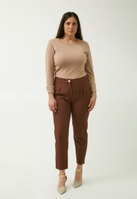 Beige lange mouw top gecombineerd met bruine, hoge taille broek met een gouden knop. Het model draagt glinsterende, puntige hakken.