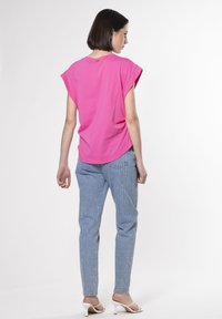 Fuchsia kortærmet skjorte med en afslappet pasform, parret med lyseblå jeans med lodrette striber og diskrete udsmykninger.