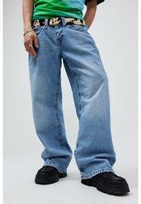 Jeans de denim azul claro, holgados y con una textura ligeramente deslavada, combinados con un zapato negro de suela gruesa y un cinturón de patrón.