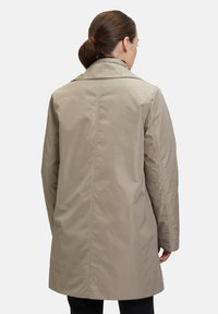 Ljus beige kappa med en strukturerad krage, långa ärmar och en rak silhuett. Tyget verkar slätt och har minimala sömmar.