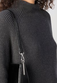 Personne portant un pull en maille côtelée gris foncé avec une sangle de sac à main en cuir embossé croco noir sur l'épaule.