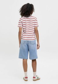Camiseta de rayas rojas y blancas con mangas cortas, combinada con pantalones cortos de mezclilla azul claro. Se lleva con calcetines crema y zapatillas deportivas.