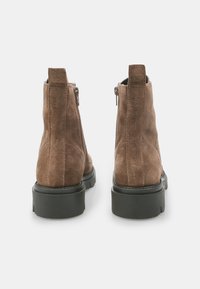 Bottines en daim marron avec une finition texturée, fermeture éclair et semelle en caoutchouc noir épaisse. La vue arrière met en avant un design épuré.