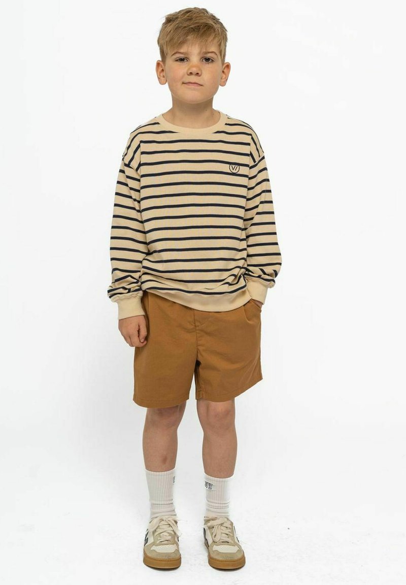 Camicia a maniche lunghe a righe beige con righe marine, pantaloni corti beige, calzini bianchi e sneakers beige con accenti più scuri. Outfit casual per bambini.
