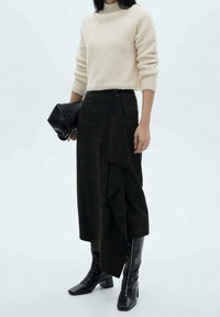 Kermainen pörröinen neule, kerroksellinen musta ruudullinen hame, jossa on laskosdetalji, ja polvipituiset mustat nahkasaappaat, yhdistettynä mustaan clutch-laukkuun.