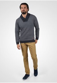 Marine-mønstret sweater med sjalskrave, parret med tan bukser og blå sneakers. Sweateren har en struktureret strik og ribbede manchetter.