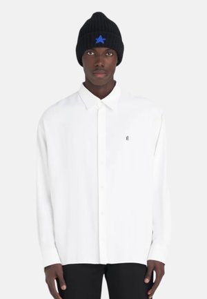 Chemise blanche à manches longues avec col et petit logo noir. Assortie à un bonnet en tricot noir à côtes avec un motif d'étoile bleue.