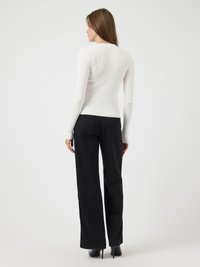 Moteris stovi nugara į mus apsivilkusi prigludusią baltą dryžuotą ilgą rankovę viršutinę dalį, juodus plačius kelnes ir juodas aukštakulnius batus.