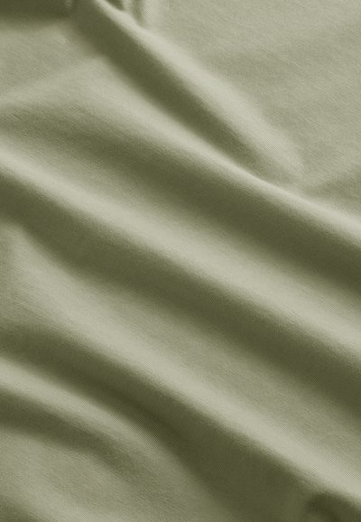 Tissu doux et vert clair avec des plis délicats et une texture lisse, montrant des variations subtiles de lumière et d'ombre.