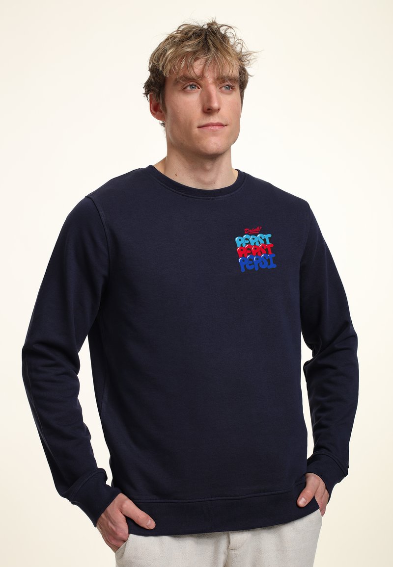 Felpa in cotone blu navy con maniche lunghe, polsini a coste e colletto a girocollo. Presenta il colorato logo "Pepsi" in testo in grassetto sul petto.