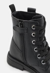 Stivale in pelle nera con design lacciato, zip laterale, occhielli metallici e suola in gomma testurizzata.