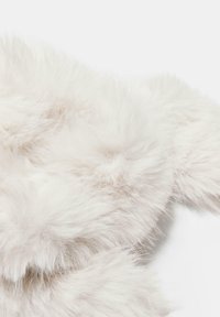 Pehmeä, pörröinen valkoinen tekokarvafarkku, jossa on pitkiä, hienoja kuituja, jotka luovat tiheän ja ylellisen tekstuurin vaalealla taustalla.