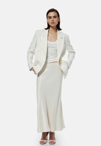 Blazer blanco con rayas sobre una blusa blanca ajustada, combinado con una falda midi de satén marfil elegante y sandalias de tacón ligeras.