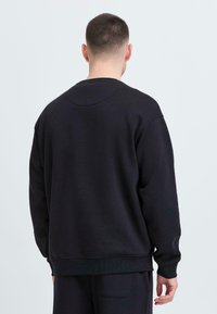 Felpa girocollo blu scuro con maniche lunghe, polsini e orlo a coste. Texture morbida, design minimalista, senza loghi o fantasie visibili.