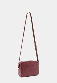 Borsa a tracolla color bordeaux con design a logo impresso, texture liscia, forma rettangolare, tracolla regolabile e dettagli in metallo dorato.