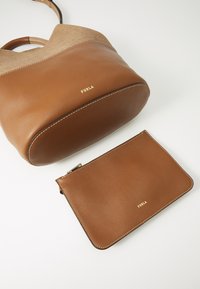 Brown leather tote bag with suede accents, featuring a curved shape and gold hardware. Includes a matching brown leather pouch with a zipper.