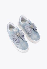 Baskets en denim bleu clair avec un grand nœud décoratif, des accents cloutés et des semelles en caoutchouc blanches. Texture douce et design décontracté.