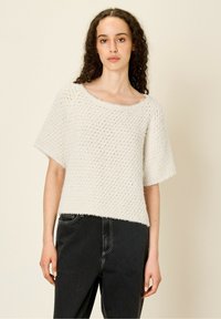 Haut en tricot blanc texturé avec un col large et des manches courtes, associé à un jean noir taille haute. Le haut présente une coupe ample et carrée.