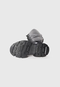 Botte en cuir noir avec semelle en caoutchouc texturé et détails à lacets, présentée au niveau du sol mettant l'accent sur la semelle et le motif de la chaussure.