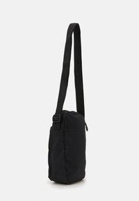 Borsa a spalla nera realizzata in tessuto resistente, dotata di una tracolla regolabile, forma rettangolare compatta e tasca con zip per lo stoccaggio.