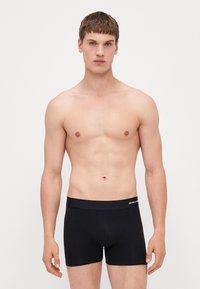 Schwarze Boxershorts aus einem glatten Material mit einem breiten, elastischen Bund, der weißen Logo-Text aufweist. Die taillierte Passform betont die Körperform.