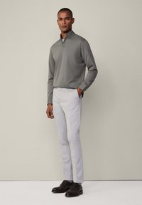 Svijetlosiva pamučna polo majica dugih rukava s ovratnikom, u kombinaciji s krojenim svijetlosivim hlačama i tamnosmešnim cipelama na vezanje. Glatka tekstura tkanine.