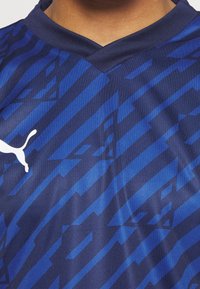 Mörkblå atletisk tröja med ett strukturerat mönster av olika nyanser av blått och en vit logotyp på vänster sida av bröstet.