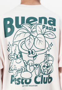 Witte shirt met korte mouwen voorzien van groene cartoonillustraties van pasta, kaas, basilicum en knoflook, met de tekst "Buena Pasta Pesto Club."