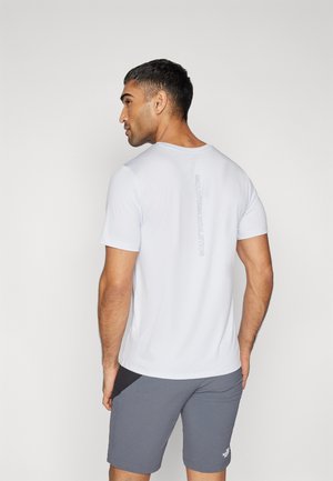 T-shirt de sport blanc à manches courtes avec un col rond. Présente un logo vertical gris "MOUNTAIN ATHLETICS" au dos. Tissu doux et léger.