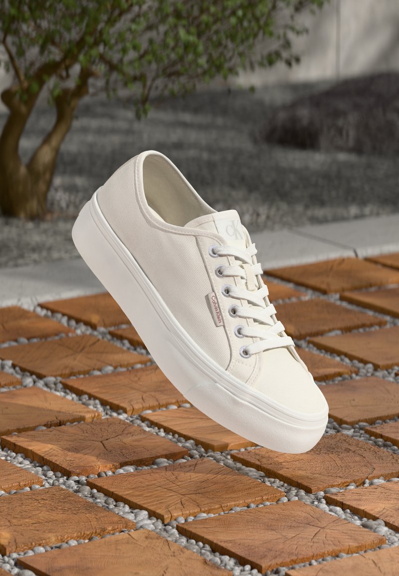 Sneakers bianchi in tela con suola in gomma, punta tonda e design con lacci. Presentano un piccolo logo sul lato e tessuto texturizzato.