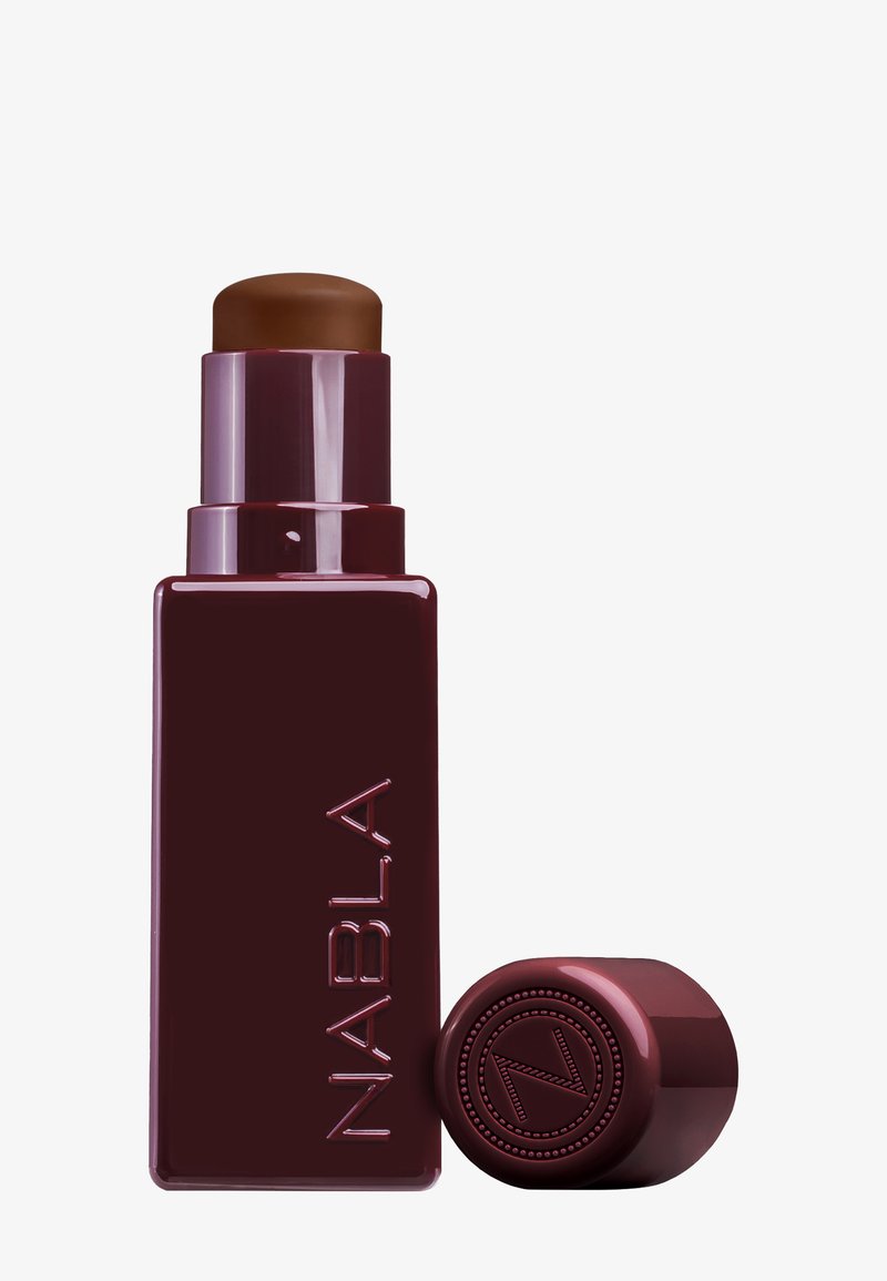 Stick de fond de teint NABLA en teinte brun foncé ; design cylindrique en plastique avec une finition bordeaux brillante et logo en relief sur le capuchon.