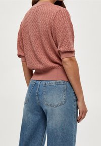 Rosa-rosa stickad tröja med en texturerad design, korta ärmar och ribbad nederkant. Matchad med högmidjade blå denimjeans.