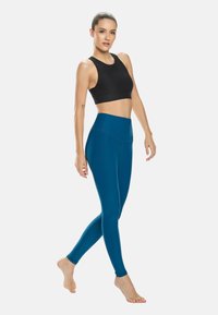 Sujeción deportiva negra y leggings azul verdoso, diseño ajustado, cintura alta, textura suave, sin patrones o herrajes visibles.