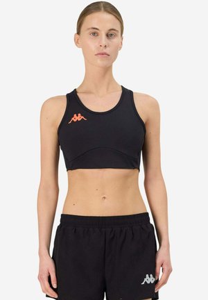 Donna snella che indossa un top sportivo nero con logo arancione e pantaloni da tuta neri larghi con logo grigio, in piedi davanti a uno sfondo bianco.