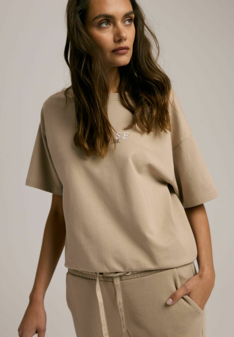 Beżowa bawełniana koszulka z krótkim rękawem i luźnym krojem, z subtelnym nadrukiem "proszę". W połączeniu z pasującymi jasnymi dresami.