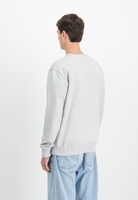 Sweatshirt grigio chiaro con colletto a giro e polsini a costine, dotato di un'etichetta rettangolare sul retro. Abbinato a jeans blu a vestibilità larga.