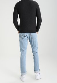 Pull sombre à encolure ronde, associé à un jean bleu clair à jambes droites et des baskets blanches, avec des revers de pantalon et des détails minimalistes.