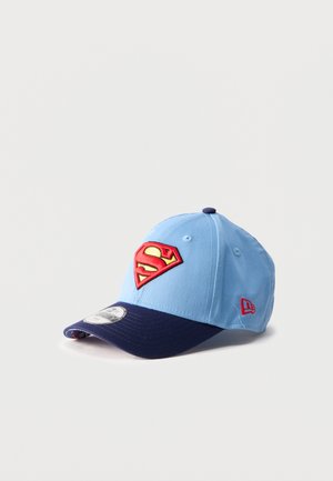 Svetlo modra in mornarsko modra baseball kapa z rdečim in rumenim Supermanovim logotipom spredaj ter rdečim logotipom New Era na strani, postavljena na belo ozadje.