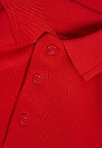 Camisa polo roja con tejido texturizado, un cuello y tres botones a juego en la tapeta. La vista en primer plano enfatiza los detalles.