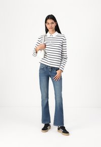 Striped long-sleeve polo shirt in white and navy, paired with blue flared jeans and black sneakers with white accents. Simple handbag in hand.