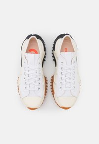 Sneakers bianchi in tela con dettagli in gomma, punte rotonde e suole spesse e frastagliate in nero e arancione. Presentano occhielli in argento e lacci bianchi.