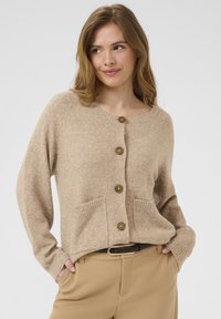 Beige adīts kardigans ar apaļu kaklu, piecām brūnām pogām un divām priekšējām kabatām. Mīksta tekstūra, brīva piegriezuma un garas piedurknes.