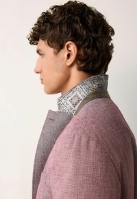 Blazer à motif pied-de-poule en rouge décoloré, avec une finition en tissu texturé. Doté d'un col à motif contrastant bleu et crème.