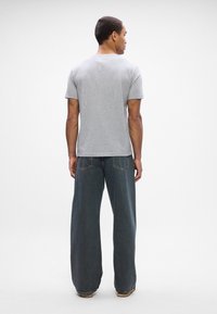 Camiseta de algodão cinza com mangas curtas, combinada com jeans escuros de corte largo, apresentando costuras em contraste e um design de perna reta.