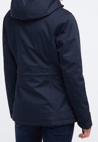 Mörkblå vattentät jacka med huva, figursydd midja och slät struktur. Inkluderar rak nederkant och uppvikta ärmar.