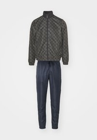 Giacca grigia scura a fantasia con colletto alto e pantaloni sportivi blu navy, dotati di vita e polsini elasticizzati, realizzati in materiale liscio e lucido.